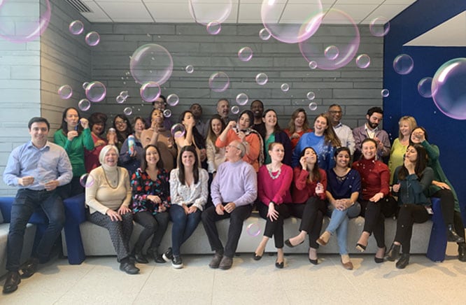 Diverse group of office professionals smiling and blowing bubbles in a modern workspace, reflecting a fun and collaborative company culture.