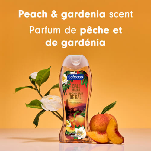 The Bali Bliss body wash bottle positioned between a fresh peach and white gardenia flowers. Text in English and French reads: Peach & gardenia scent. Parfum de pêche et de gardénia.