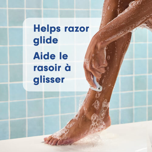 A close-up of a person shaving their leg in the shower with a rich pink lather. Text in English and French: Helps razor glide, Aide le rasoir à glisser.