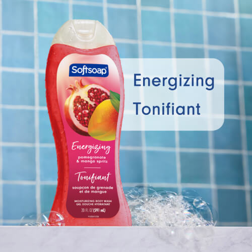 A bottle of Softsoap "Pomegranate & Mango Spritz" in a blue-tiled shower, surrounded by bubbles. The text, in English and French, reads: "Moisturizing body wash" / "Gel douche hydratant."
