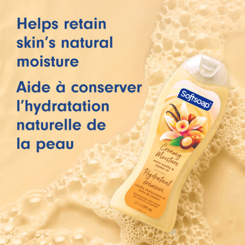 The Warm Vanilla and Jojoba Oil bottle tilted against a warm, golden-yellow background covered in soapy suds. Text reads "Helps retain skin’s natural moisture" and "Aide à conserver l’hydratation naturelle de la peau."